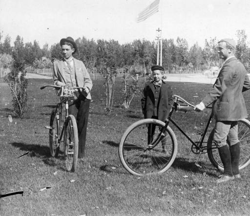Three people standing in a field with bicycles.