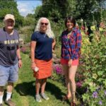 Three people standing in a garden with flowers.