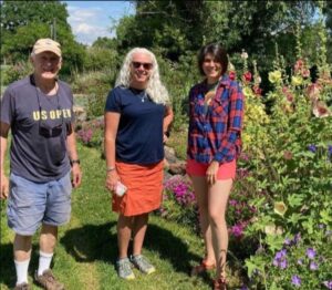 Three people standing in a garden with flowers.