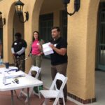 A man standing next to two women in front of tables.